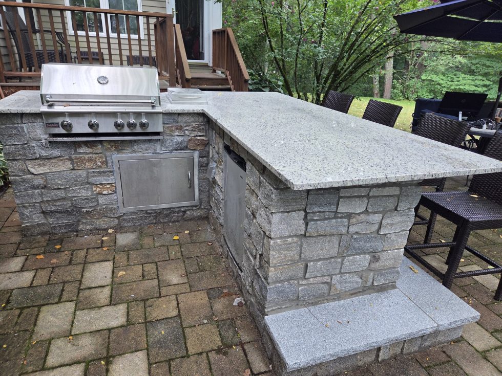 Stone-veneer outdoor kitchen with built-in grill, side burner, mini-fridge, and storage.