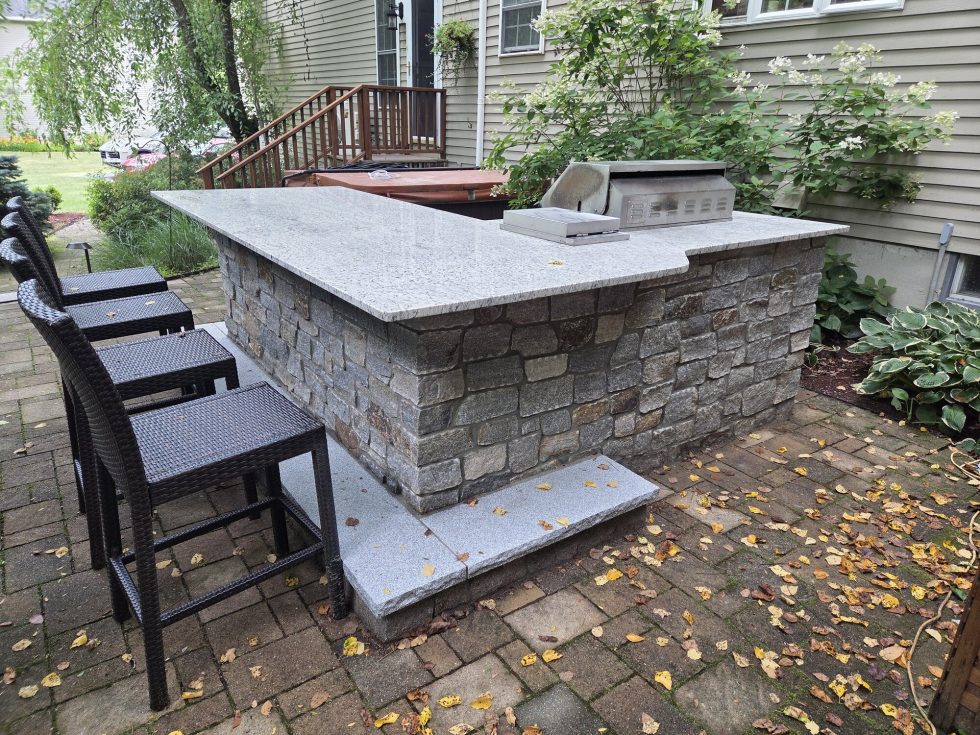 Outdoor living bar with stone veneer, solid-surface countertop, and restored paver patio.